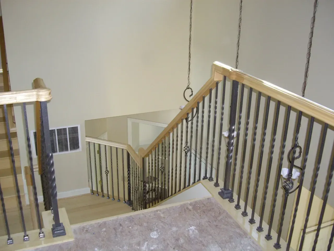 Staircase with wooden handrails and black metal balusters; beige walls.