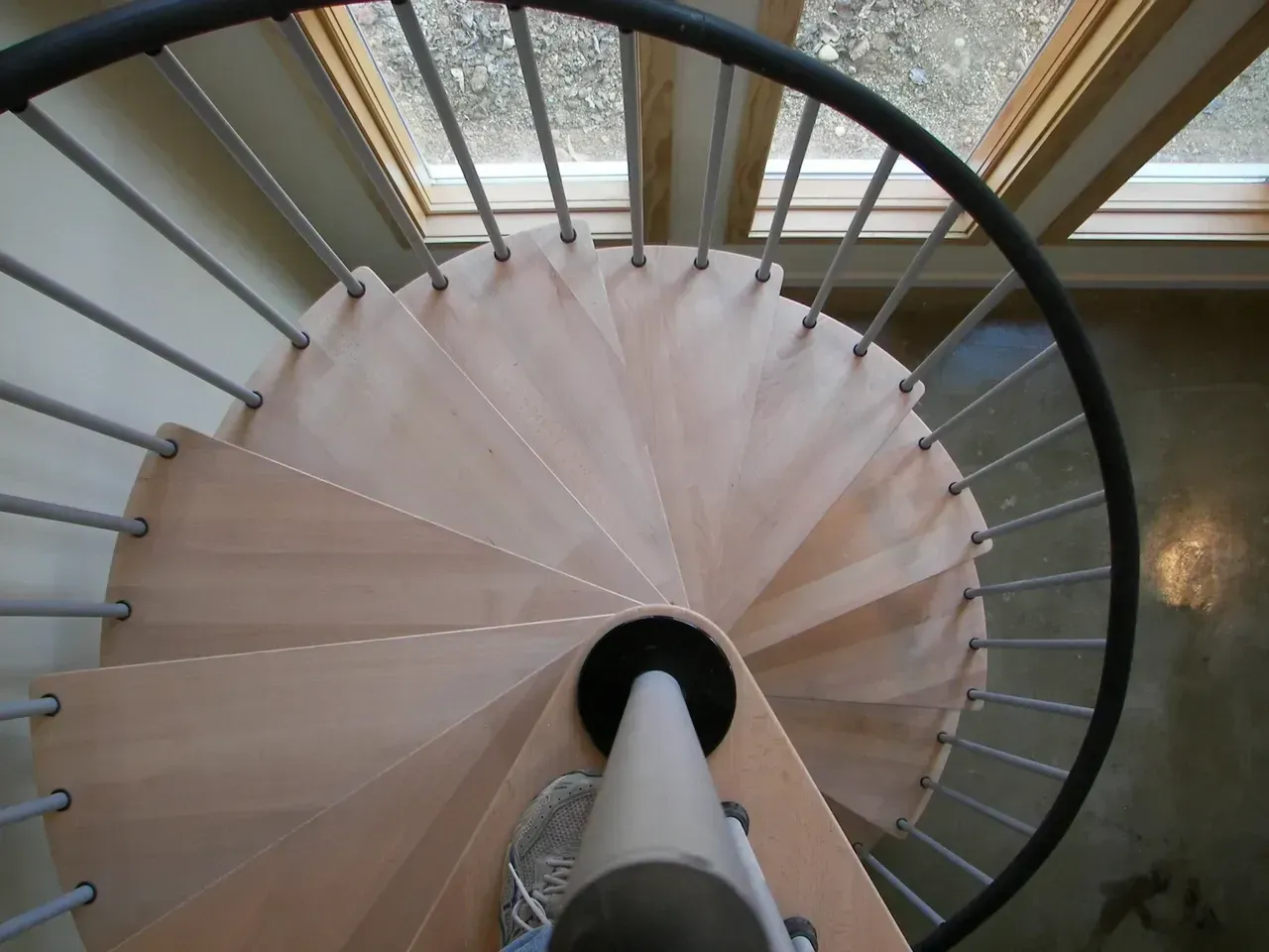 Spiral staircase with light wooden steps, metal railings, and a central support column.