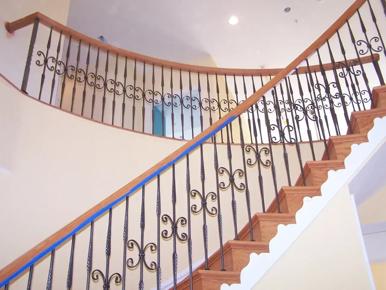 Wooden staircase with black wrought-iron railing against a cream-colored wall.