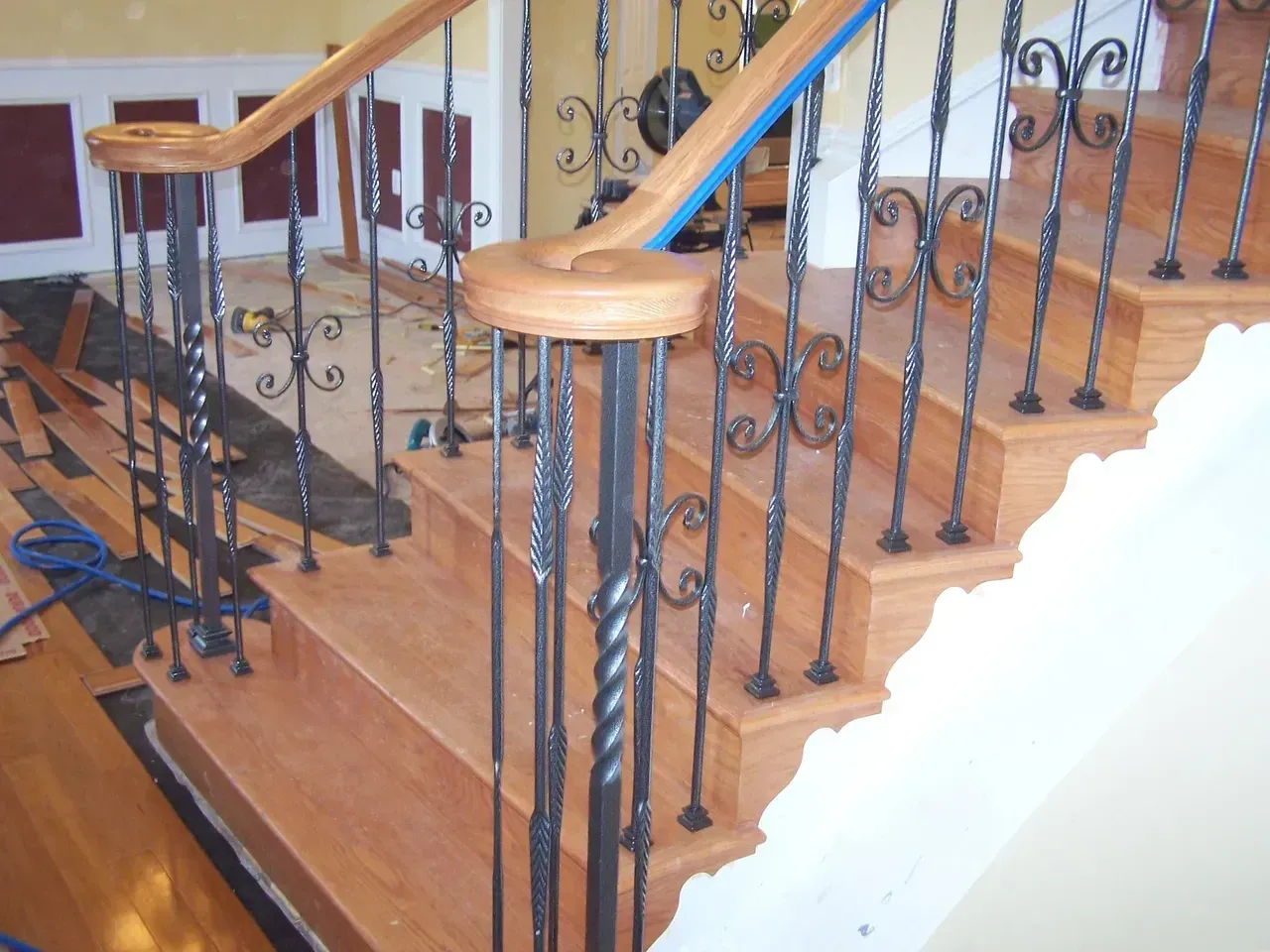 Wooden staircase with ornate wrought iron balusters and wood handrails.