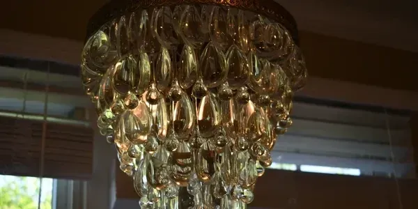 Crystal chandelier hangs from the ceiling; a window with blinds is in the background.