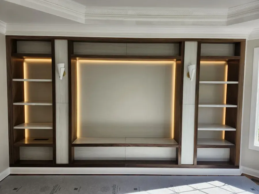Built-in wooden wall unit with shelves, lighting, and a central panel. White and brown tones.