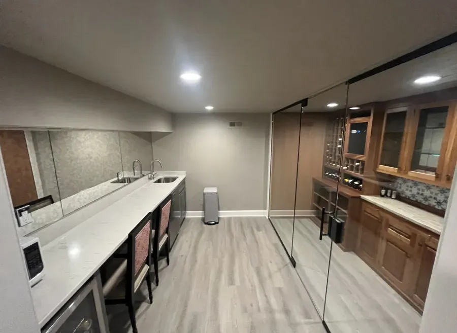 Basement bar with countertop, stools, cabinetry, and a mirrored wall.