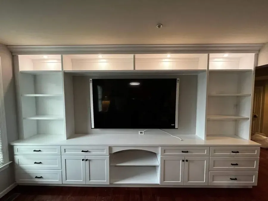 White built-in entertainment center with shelves, cabinets, and a mounted TV.