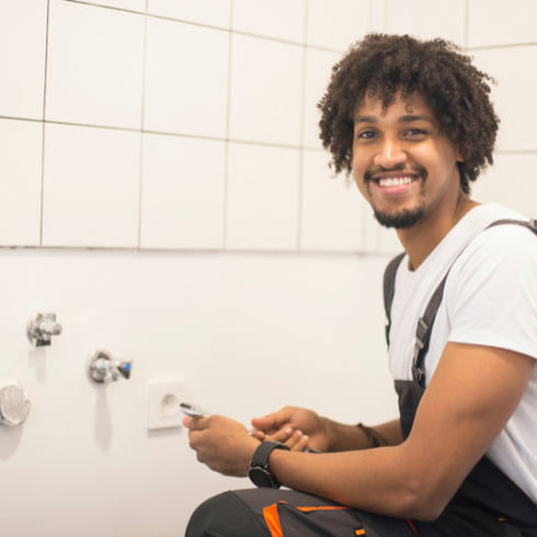 Plumber smiling while kneeling in front of plumbing faucets