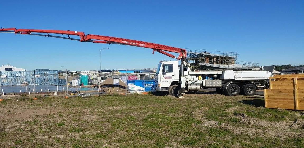 A White Truck With a Red Crane Attached to It is Parked in a Grassy Field — Tweed Coast Concrete Pumping in Chinderah, NSW