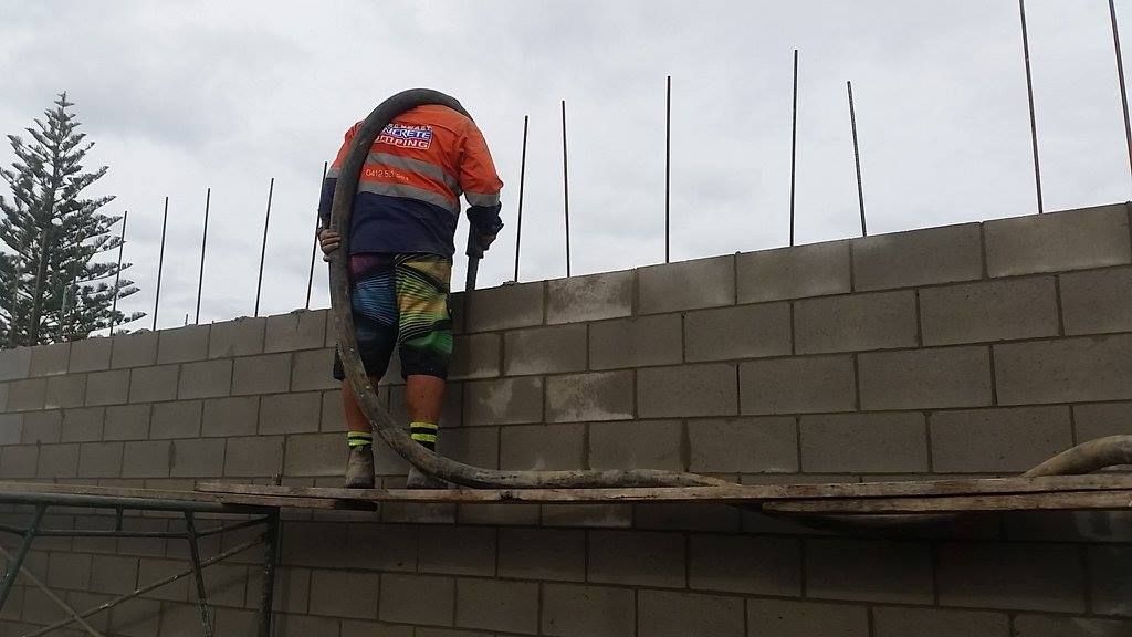 A Man is Standing on a Scaffolding on Top of a Brick Wall — Tweed Coast Concrete Pumping in Chinderah, NSW