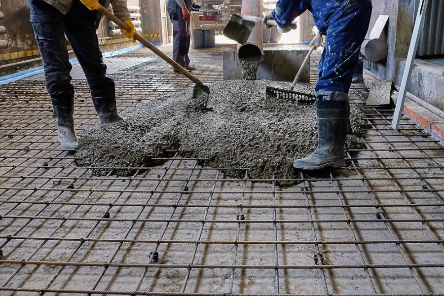 Two Construction Workers Are Pouring Concrete on a Steel Mesh Floor — Tweed Coast Concrete Pumping in Banora Point, NSW