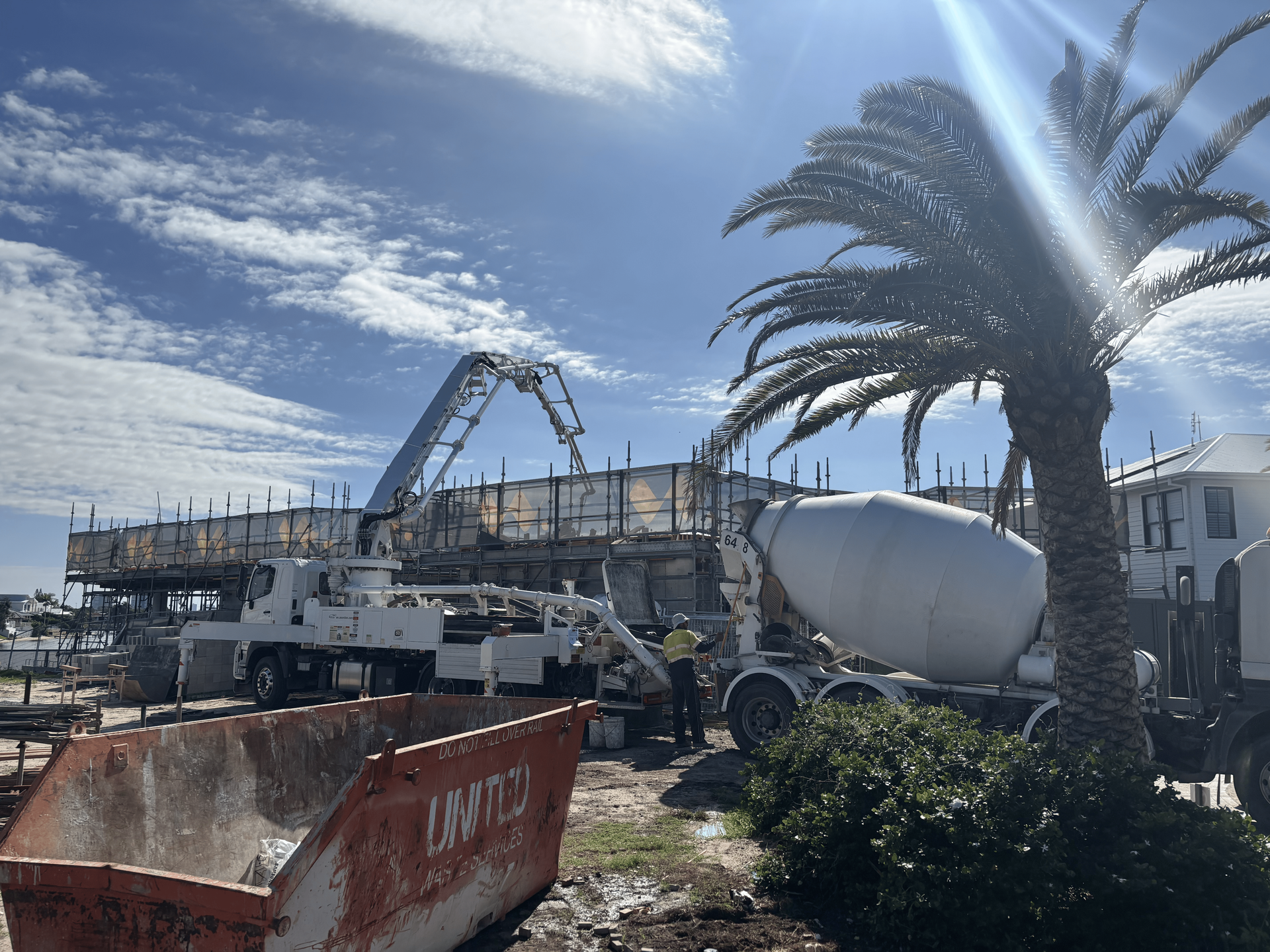 Construction site with concrete truck and pump filling wooden forms under a bright blue sky.