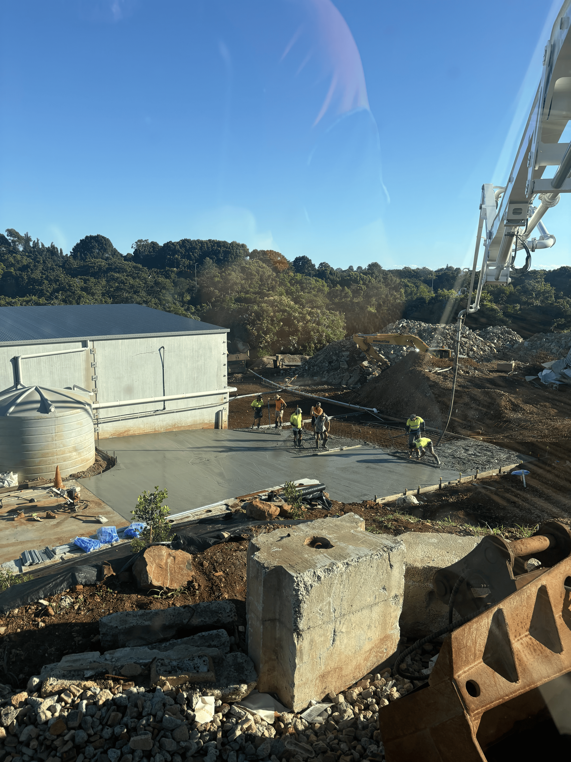 Construction site with workers in yellow vests. Concrete being poured near a building, clear sky.