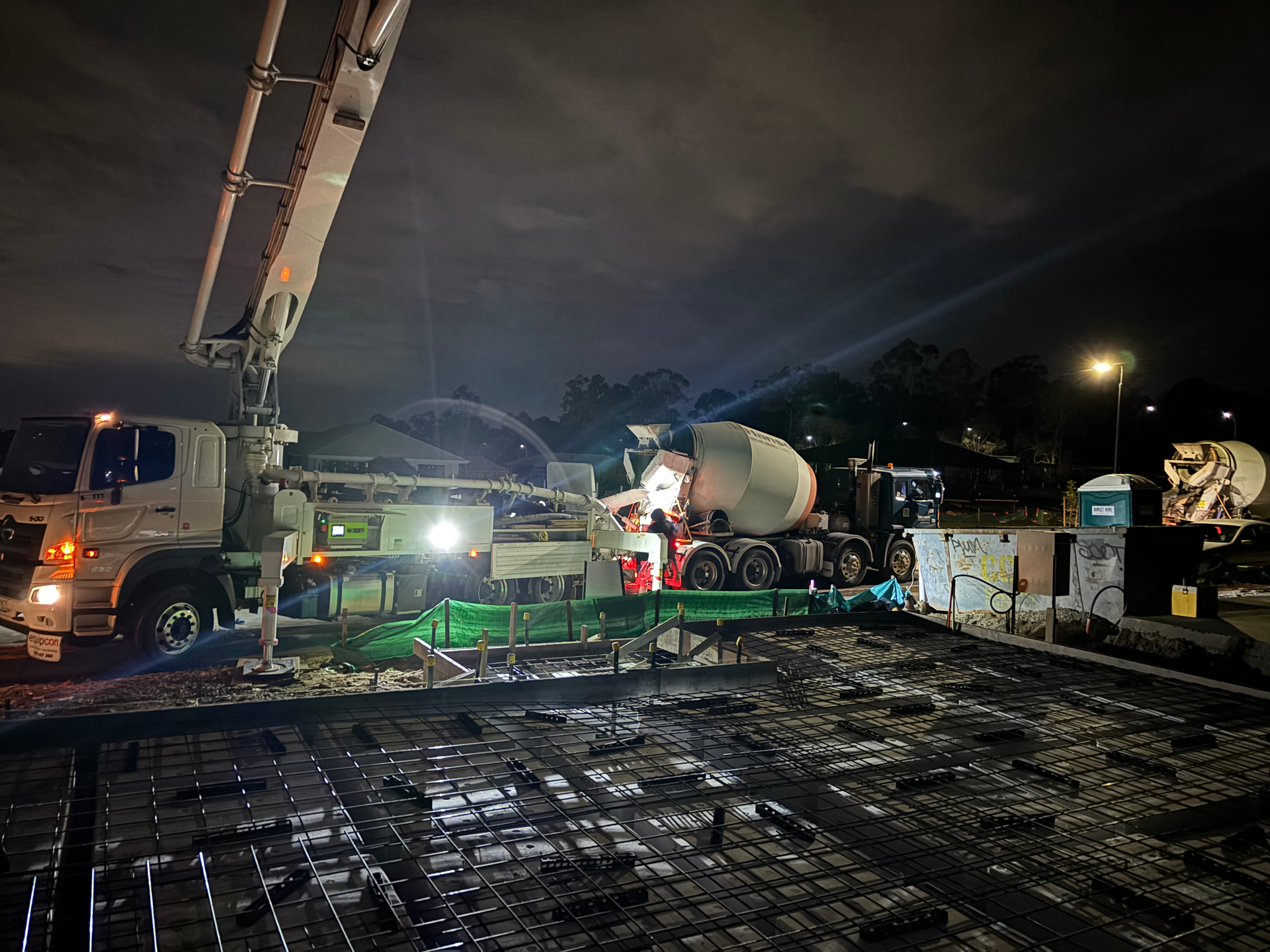 Concrete pour at night, truck with boom arm dispenses concrete onto rebar framework.