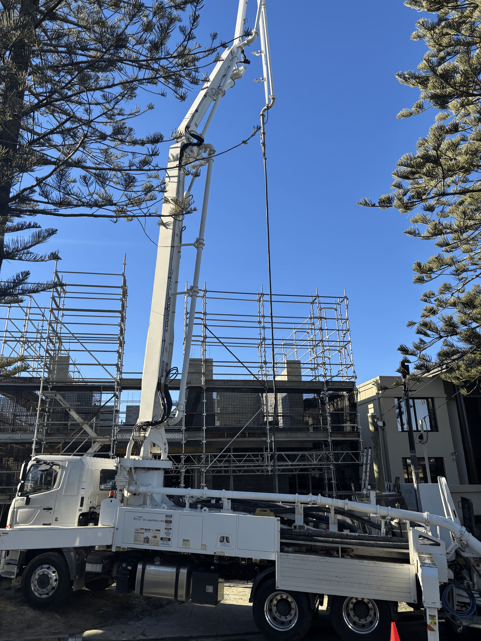 White concrete pump truck with extended boom pumping concrete on a building under construction, blue sky.