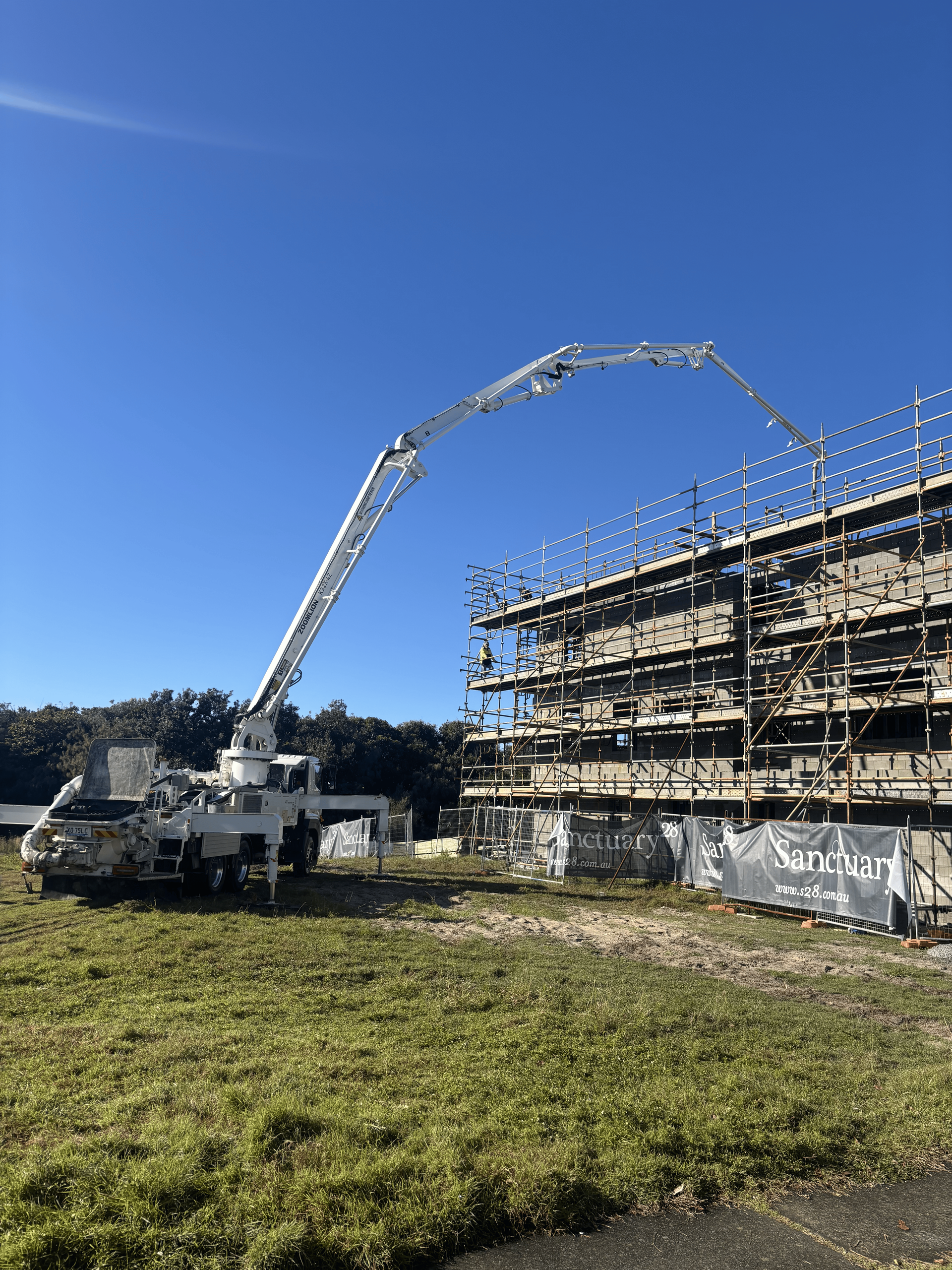 A concrete pump truck reaching to pour concrete on a building under construction with scaffolding.