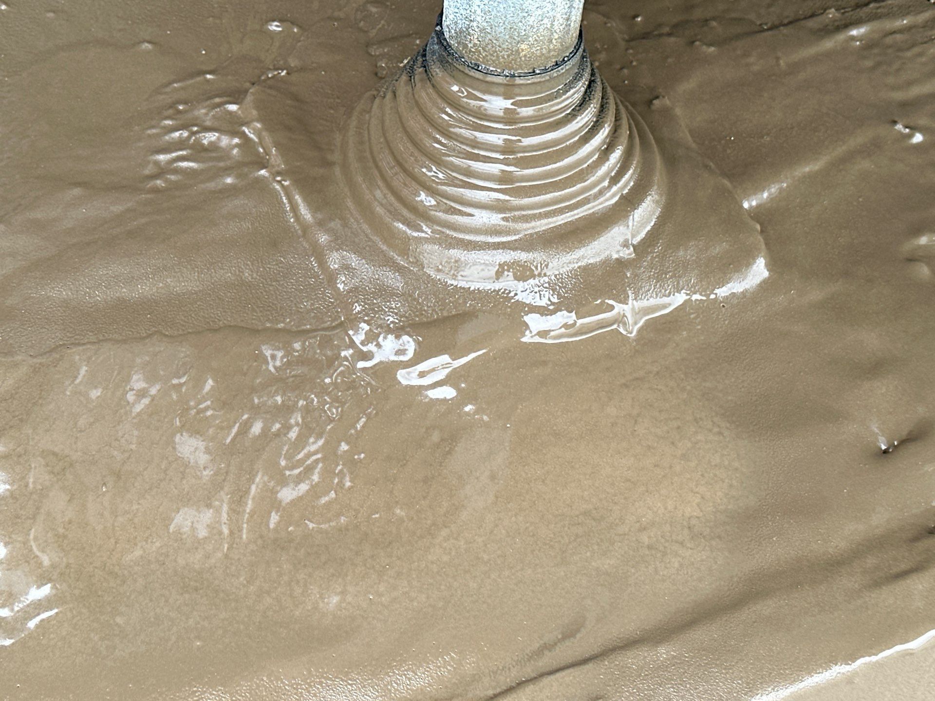 Muddy ground surrounding a cylindrical pipe. The mud is swirling and wet.