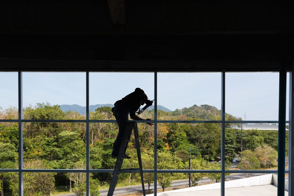 Worker on a Ladder Cleaning Large Indoor Windows — ALUBEST Windows & Doors In Southport, QLD