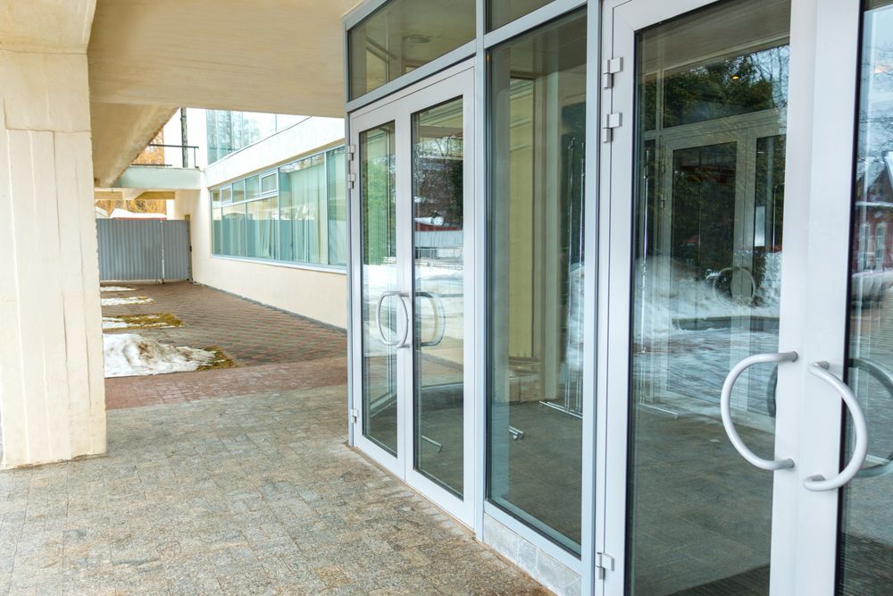 Glass Entrance Doors Along a Covered Outdoor Walkway Beside a Building — ALUBEST Windows & Doors In Southport, QLD