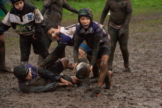 Un gruppo di ragazzi gioca a rugby nel fango.