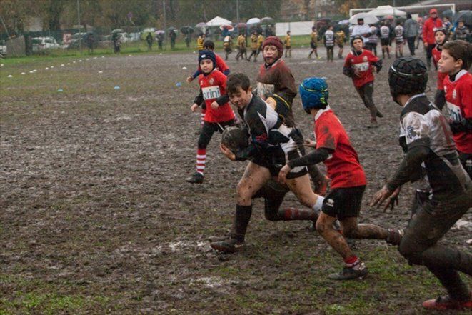 Un gruppo di ragazzi gioca a rugby su un campo fangoso.