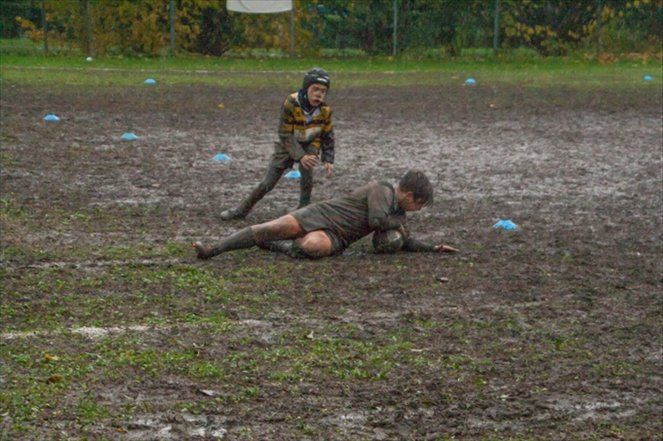 Un ragazzino sta giocando a rugby nel fango su un campo fangoso.