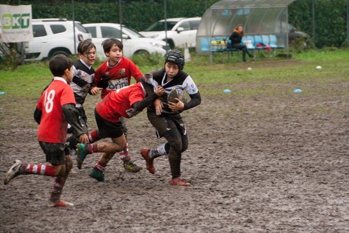 Un gruppo di ragazzi gioca a rugby su un campo fangoso.
