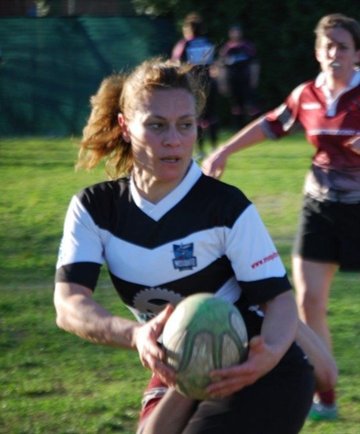 Una donna con una maglietta a righe bianche e nere tiene in mano una palla da rugby