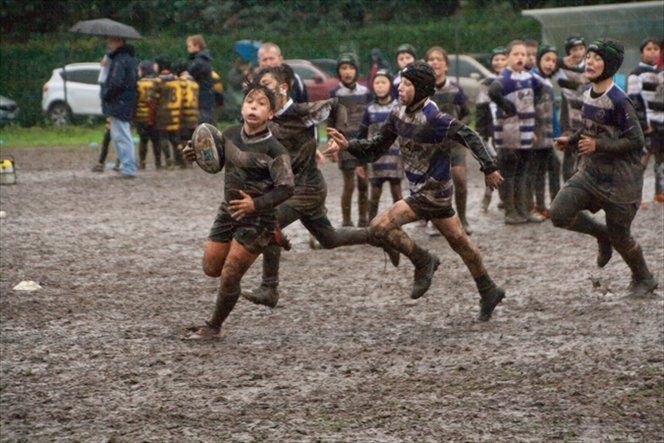 Un gruppo di ragazzi gioca a rugby su un campo fangoso.