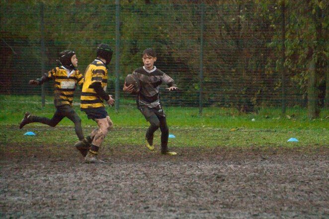 Un gruppo di ragazzi gioca a rugby su un campo fangoso.