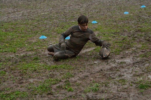 Un ragazzino è inginocchiato nel fango con in mano un pallone da calcio.