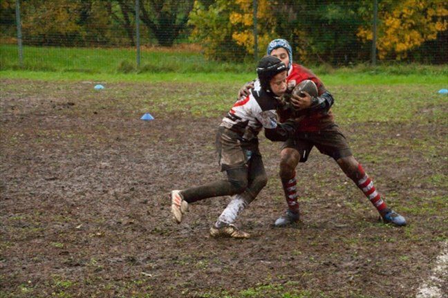 Due ragazzi giocano a rugby su un campo fangoso.