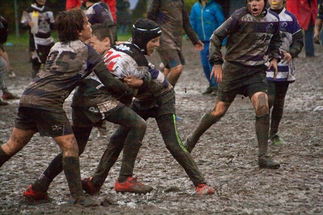 Un gruppo di ragazzi gioca a rugby nel fango.