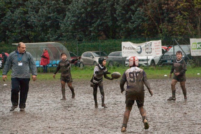 Un gruppo di ragazzi gioca a rugby su un campo fangoso.