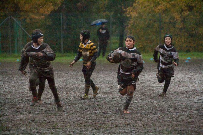 Un gruppo di ragazzi gioca a rugby sotto la pioggia su un campo fangoso.
