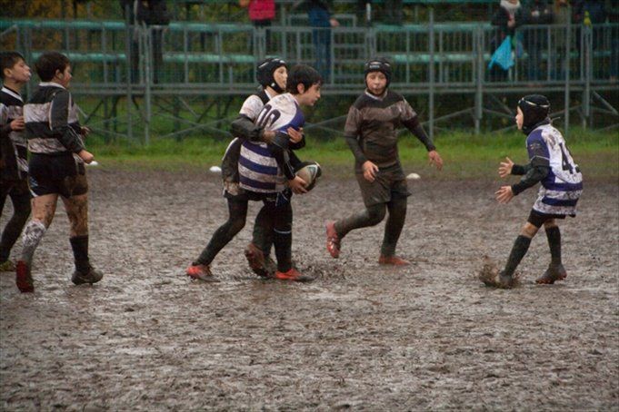 Un gruppo di ragazzi gioca a rugby su un campo fangoso.