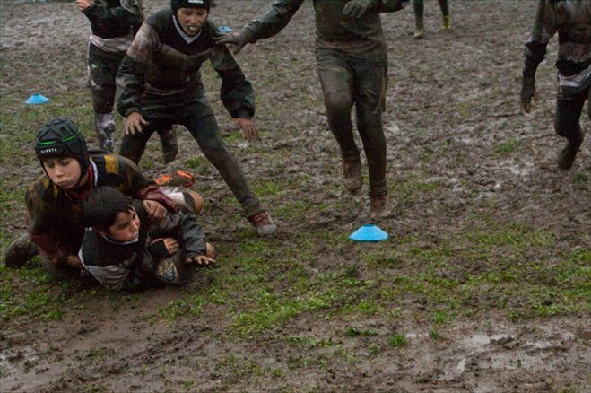 Un gruppo di bambini sta giocando a rugby nel fango.