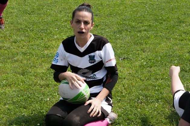 Una donna è seduta sull'erba e tiene in mano una palla da rugby.