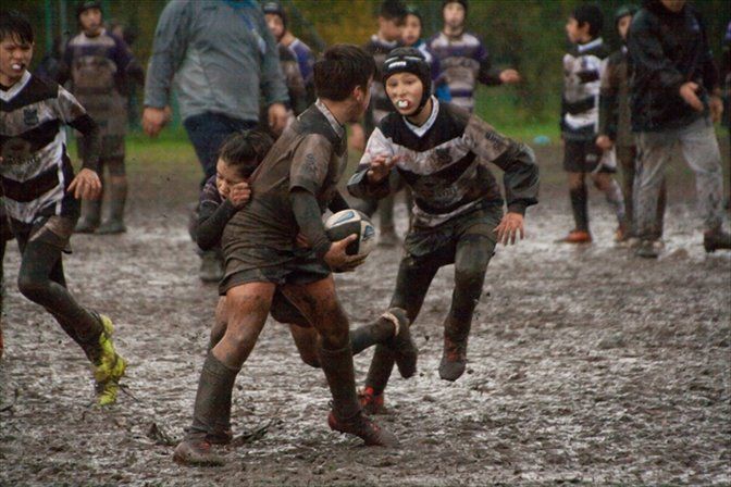 Un gruppo di ragazzi gioca a rugby su un campo fangoso.