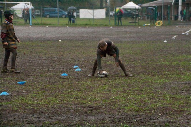 Due bambini giocano a calcio sotto la pioggia in un campo fangoso.