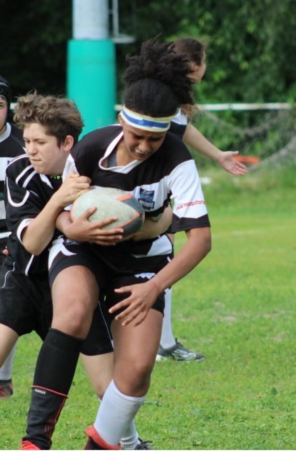 Una ragazza che indossa una fascia con il numero 5 sopra tiene in mano una palla da rugby