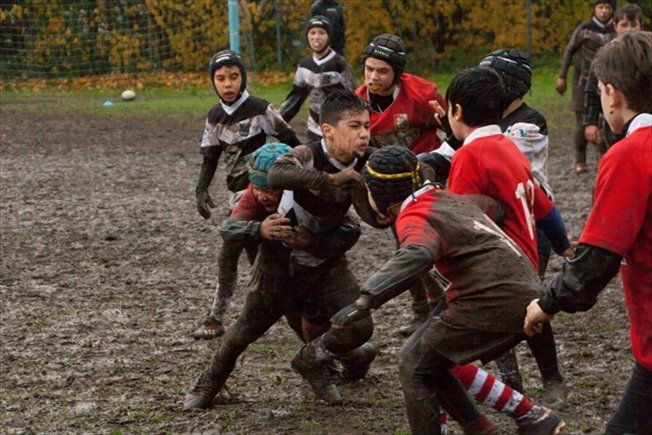 Un gruppo di ragazzi gioca a rugby su un campo fangoso.