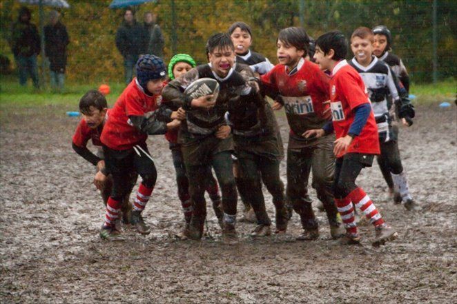 Un gruppo di ragazzi gioca a rugby su un campo fangoso.