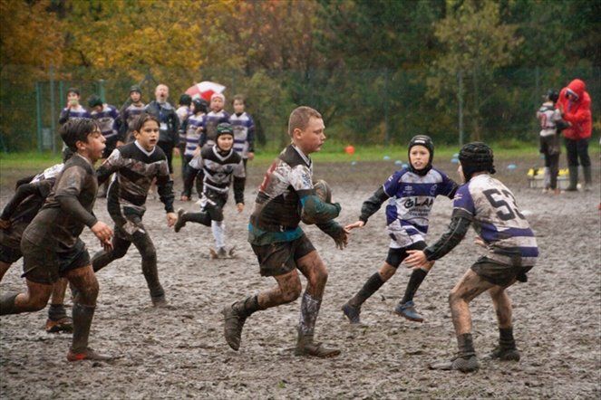 Un gruppo di ragazzi gioca a rugby su un campo fangoso.