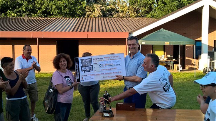 Un gruppo di persone è in piedi attorno a un tavolo e tiene in mano un assegno di grossa entità.