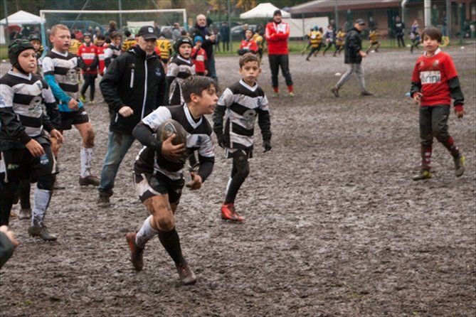 Un gruppo di ragazzi gioca a rugby su un campo fangoso.