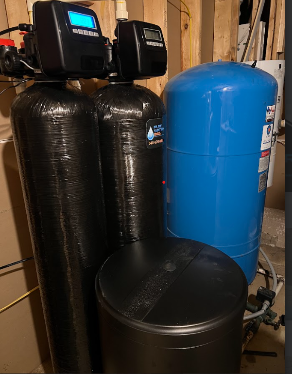 Water filtration system: two black tanks with digital displays, a blue tank, and a black brine tank in a utility room.