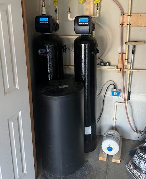 Water softener system in a garage; black tanks, digital displays, and salt storage.