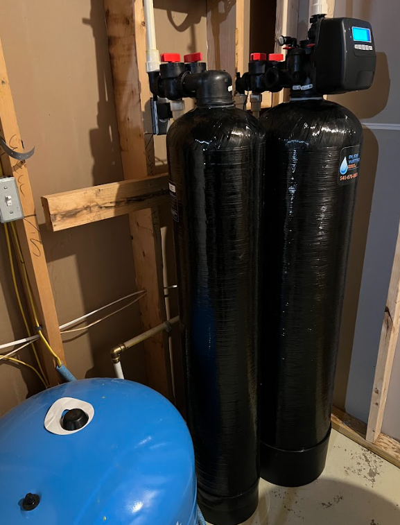 Water filtration system with two black tanks, blue tank, and control panel, installed in a basement.