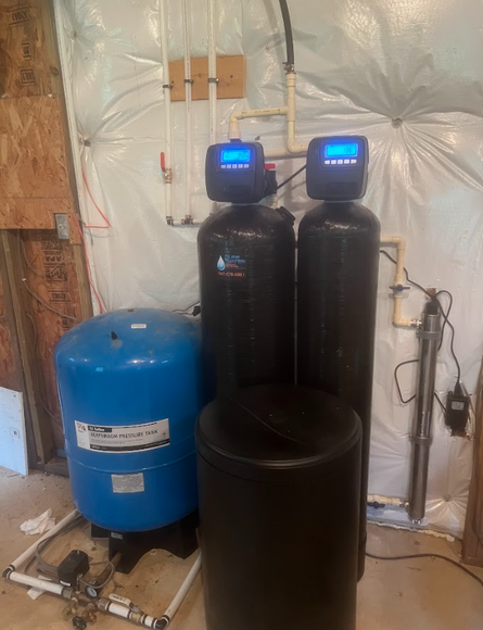 Water treatment system in a basement with blue pressure tank, black tanks, and digital displays.