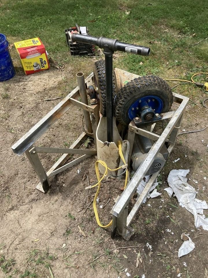 A homemade winch on wheels, likely used for pulling something. Gray metal frame, black handle, blue wheel rims.