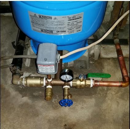 Water well pressure tank with pipes, gauges, and valves in a basement.