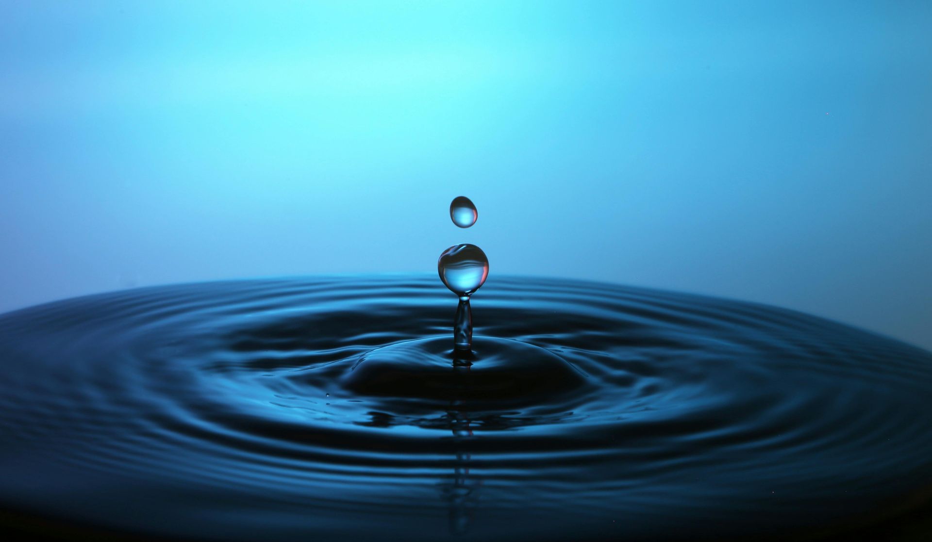 Water drop splashes into water, creating ripples, blue background.